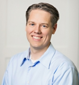 Caucasian male in light blue shirt, smiling at camera