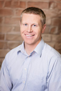 Caucasian male in light blue shirt, smiling at camera